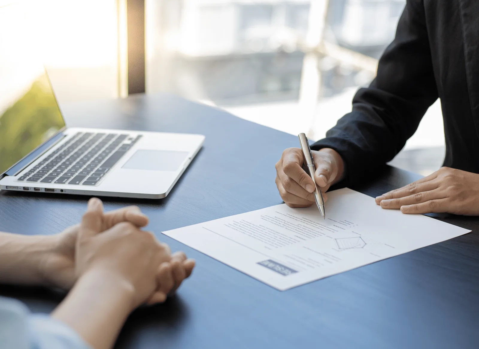 Entrevista de emprego com um currículo e um portátil em cima da mesa, a representar a comparação entre duas propostas de emprego.